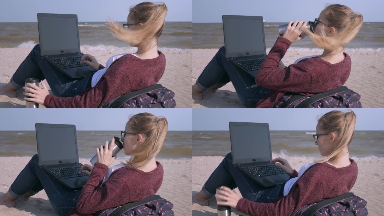 这位年轻帅气的女士一边用笔记本电脑工作，一边在夕阳下的沙滩上喝着咖啡。日落时分，年轻的商人在海滩上工