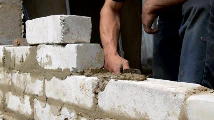 男性建筑商在水泥和站立的墙壁上铺设白砖