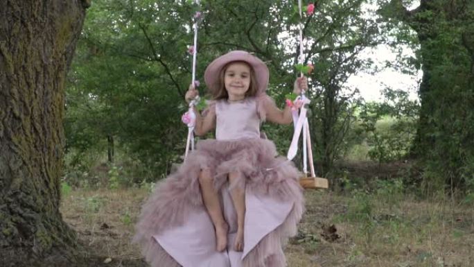 可爱的小女孩，穿着漂亮的粉色连衣裙，骑着秋千