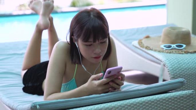 年轻的亚洲千禧一代女性从智能手机听音乐，在游泳池放松，夏天和生活方式的概念