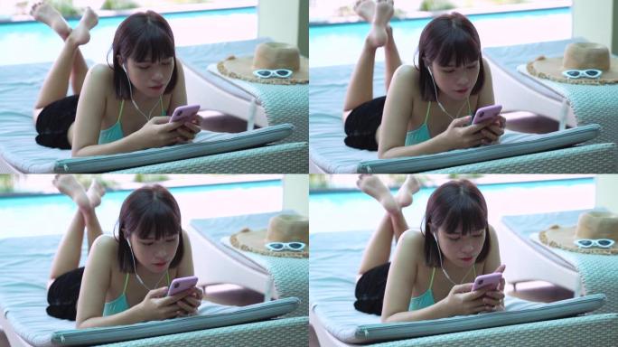 年轻的亚洲千禧一代女性从智能手机听音乐，在游泳池放松，夏天和生活方式的概念