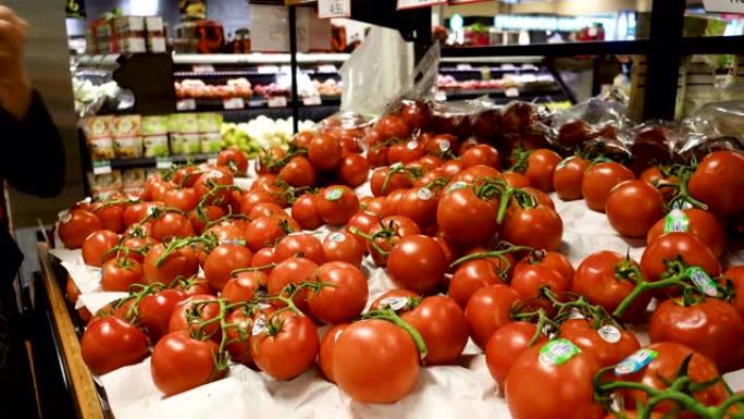 女人从超市的展示中选择新鲜西红柿。