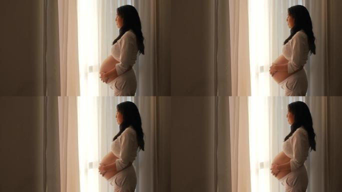 怀孕美丽的拉丁美洲妇女站在窗外看着她的肚子，剪影