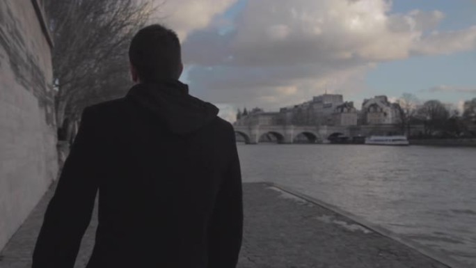 英俊的年轻沮丧的男人在午后的巴黎冬天的塞纳河畔行走，对他的前女友悲伤地思考。中枪。后视图。