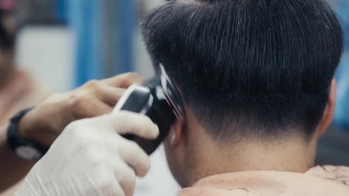 理发师的特写在理发店剪掉亚洲男人的头发。理发师的手在工作过程中。