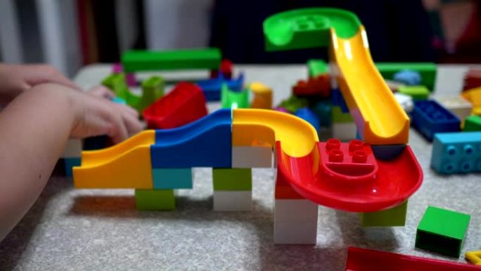 小孩子在玩积木制成的轨道。室内有许多彩色塑料玩具。