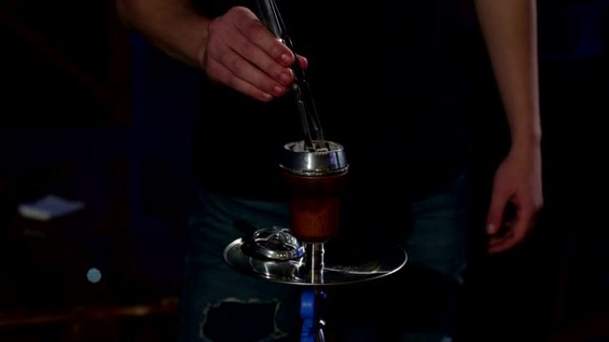 一名男子的特写镜头在黑暗的水烟酒吧的水烟里换了烧焦的煤。