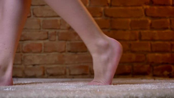在砖墙背景上的毛茸茸的地毯上，女性双腿向左缓慢行走的特写镜头。