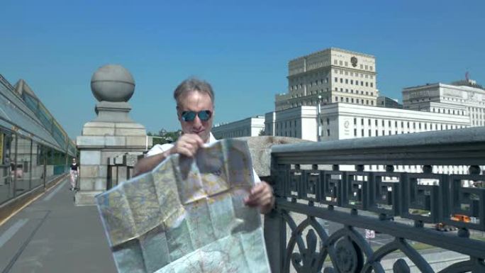 一个穿着白衬衫的男人站在桥上，看着城市的纸质地图
