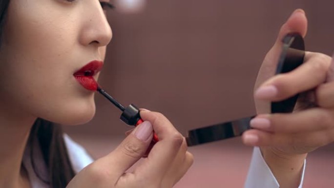 美丽的日本女孩用红色唇膏涂嘴唇。人看起来很棒。