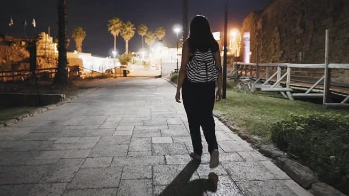 年轻女子走在凯撒利亚老城，夜景拍摄。黑发女人走在古城废墟中美丽的地方。