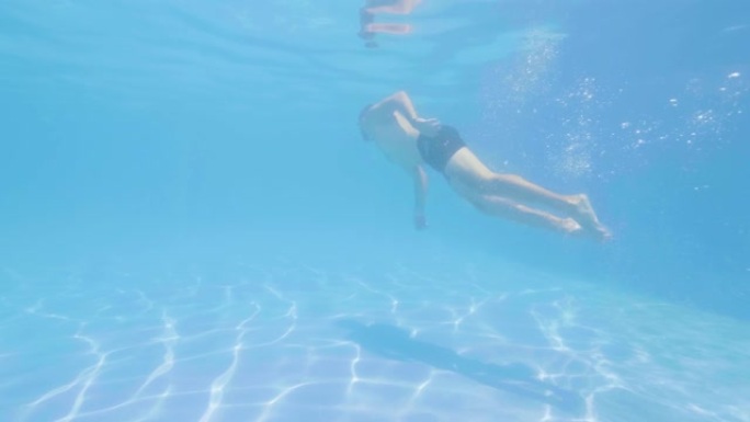 运动员男子在游泳池的蓝色水中跳跃。男子游泳者穿着护目镜潜水，在清水漂浮池下游泳。
