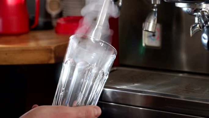 咖啡师将热蒸汽引导到空玻璃杯中。热拿铁的制备过程