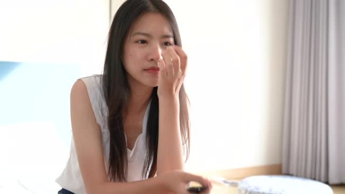 万圣节假期看恐怖电影的亚洲年轻女子坐在床上恐惧反应在酒店房间。