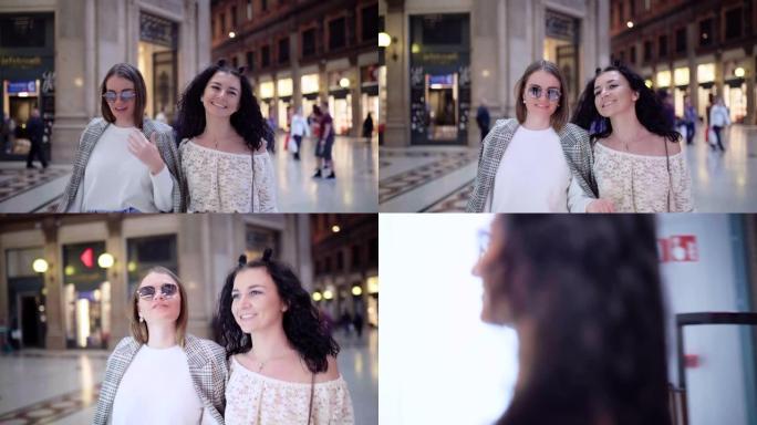 两个快乐的女孩走在购物中心，微笑着。有吸引力的女性谈论他们成功的购物日