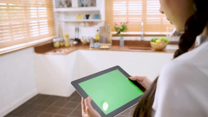 女人使用绿屏平板电脑应用程序进行家庭控制在家里的厨房里打开灯。智能家庭自动化控制概念。