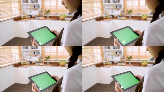 女人使用绿屏平板电脑应用程序进行家庭控制在家里的厨房里打开灯。智能家庭自动化控制概念。