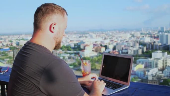 泰国芭堤雅-2019年5月12日: 男性在屋顶的咖啡馆里用笔记本电脑工作，可以看到美丽的全景。男人喝