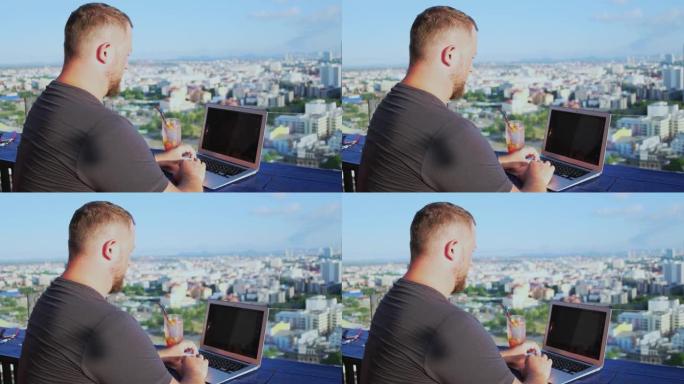泰国芭堤雅-2019年5月12日: 男性在屋顶的咖啡馆里用笔记本电脑工作，可以看到美丽的全景。男人喝