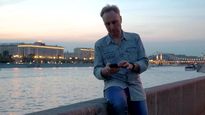 中年男子黄昏时在堤岸使用手机