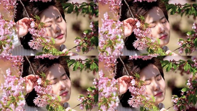 穿着白色衣服的美丽中国年轻女孩在微风中闭上眼睛，享受阳光明媚的春天，粉红色的樱花森林背景，4k电影，