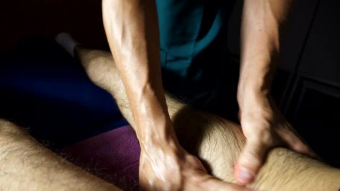 俯视图按摩师的男性手在沙龙做治疗年轻运动员的脚。专业按摩师的手臂按摩躺在客厅按摩台上的运动员的腿。慢
