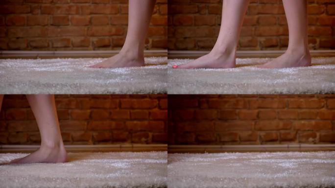 在砖墙背景上，女性双腿在毛茸茸的地毯上缓慢行走的特写镜头。