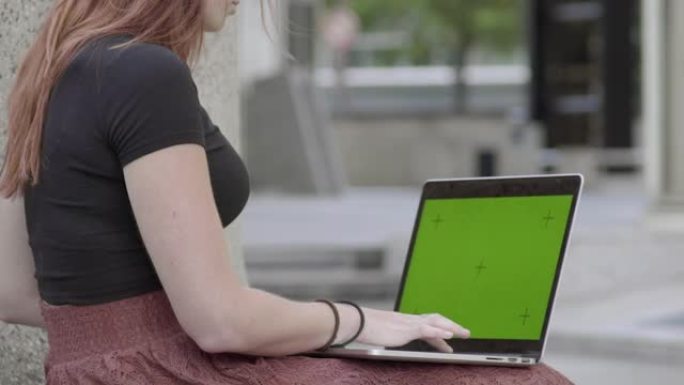 可爱的女人在户外用笔记本电脑。模拟绿屏。查看手机上的验证码，然后在internet上购买产品。在商务