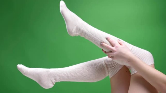 穿着可爱的白色袜子的女性少女腿的特写镜头，嬉戏地移动，背景孤立在绿色上。女孩穿上她的膝盖袜子