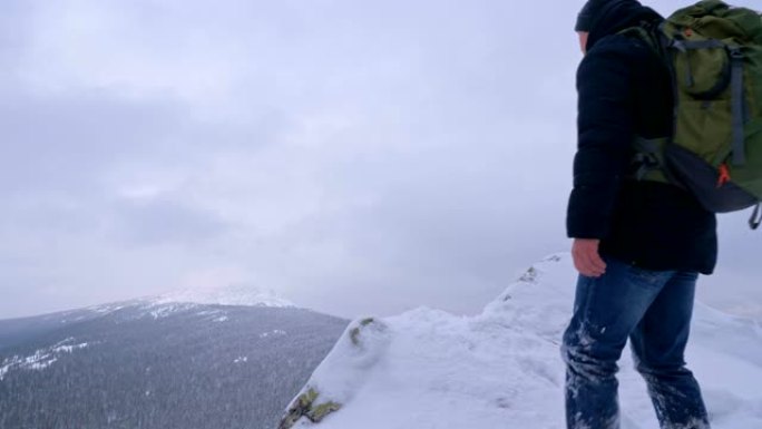 一个年轻人，一个游客，站在白雪皑皑的山边，敬佩山顶。