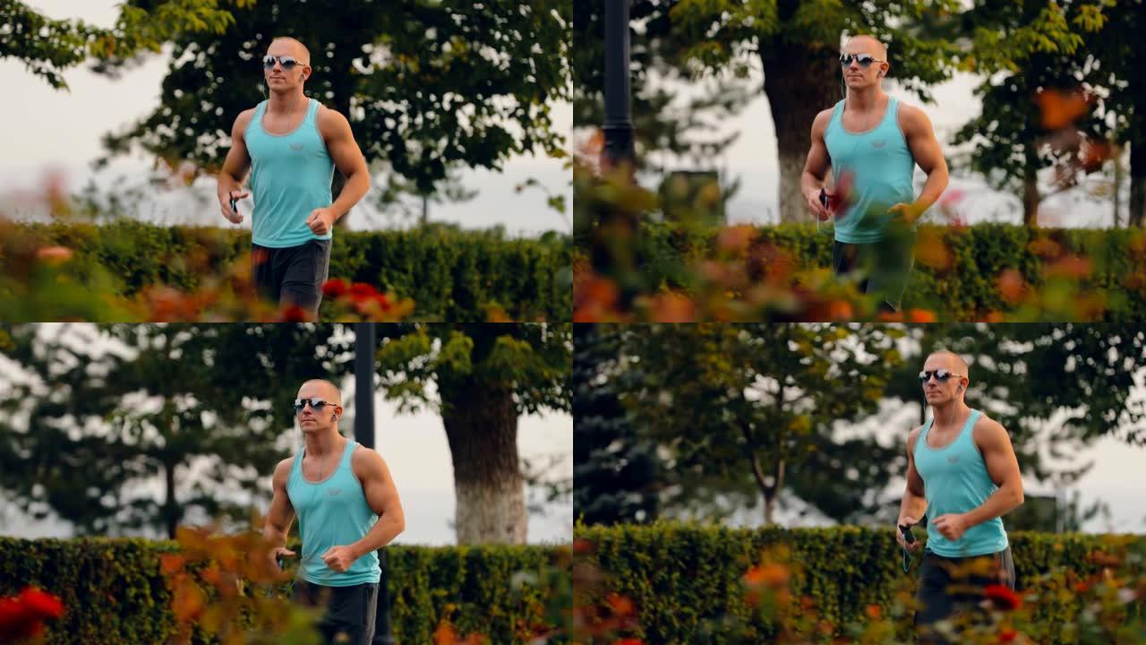 英俊的男人在公园里跑步，夏天训练。运动员戴着眼镜和耳机跑步。