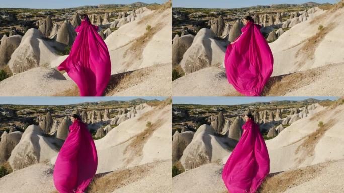 穿着紫色长裙的女孩站在卡帕多西亚的一块岩石上
