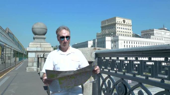 一个穿着白衬衫的男人站在桥上，看着城市的纸质地图