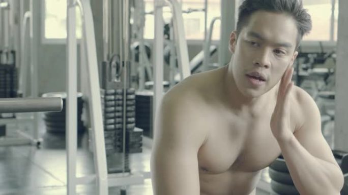 英俊的亚洲男人在健身房锻炼后肌肉发达，疲惫和疲惫，男性在锻炼后出汗休息，身体强壮，健美健康。
