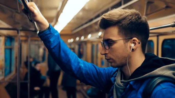 乘客坐在车里，抓住铁轨，戴着耳机听音乐。年轻人坐地铁，用手摸他的头发。