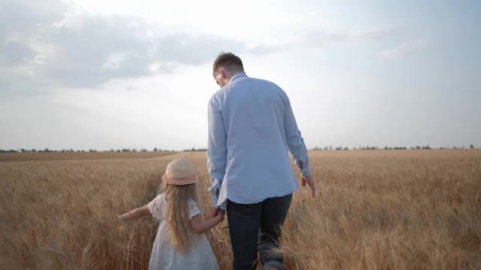 一家人在田间散步，年轻的父亲和小女儿在收获的成熟的麦田里抚摸着阳光灿烂的金色小穗