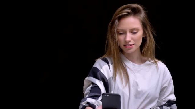 穿着白色t恤的金发高加索长发女孩的肖像很高兴在黑色背景的智能手机上的视频聊天中交谈。