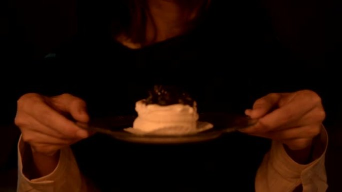 一个心满意足的女孩魔术师在黑暗的房间在烛光下变魔术自己一个蛋糕的特写。拿着一盘蛋糕低调的现场摄像机。