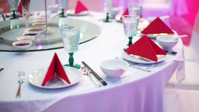 为婚宴或活动派对设置的桌子，配有圆桌会议，客人可以在室内用红色餐巾纸、陶器和带白色桌布的眼镜。