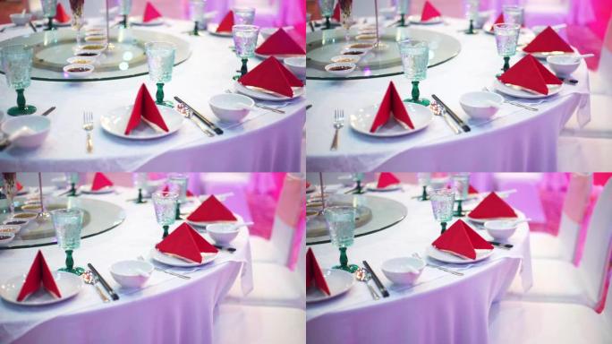 为婚宴或活动派对设置的桌子，配有圆桌会议，客人可以在室内用红色餐巾纸、陶器和带白色桌布的眼镜。