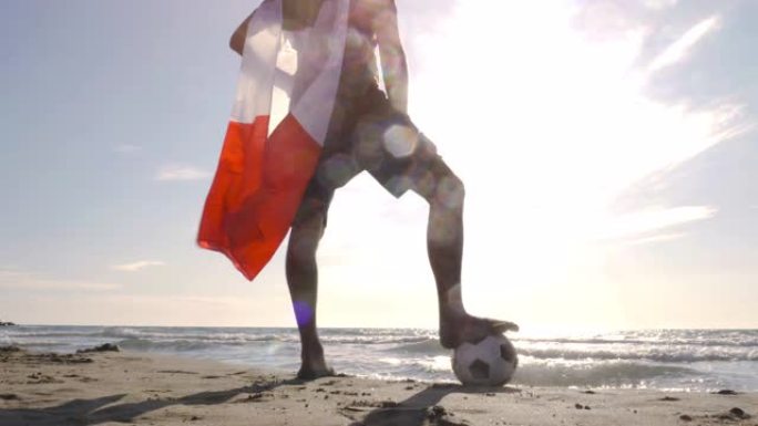 戴着意大利国旗的年轻人在海边的沙滩上站着足球，看着日落时海滩上的海洋摄像机steadycam万向节旋