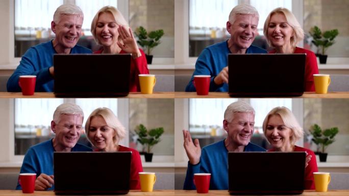 老年幸福夫妇的特写镜头在笔记本电脑上进行视频通话，桌上放着茶杯，在舒适的公寓里在室内挥手致意