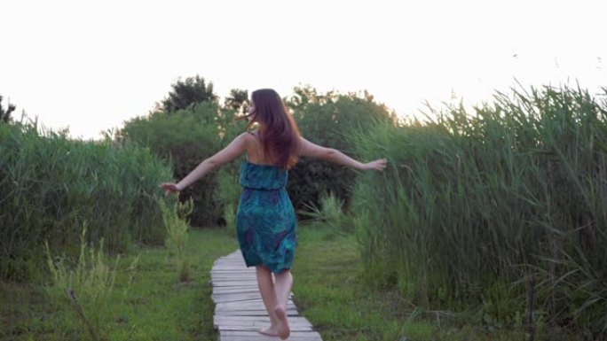 迷人的女孩赤脚在户外的木桥上奔跑，在高绿草丛中享受自然
