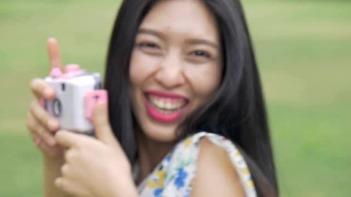慢动作美丽的年轻亚洲女子喜欢在公园户外用玩具相机拍照。
