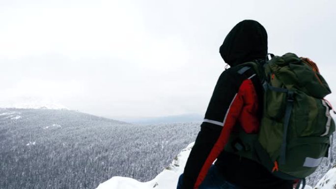 一个年轻人，一个游客，站在白雪皑皑的山边，敬佩山顶。