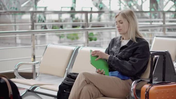 乘客女孩正坐在机场候车室里从袋子里拿平板电脑