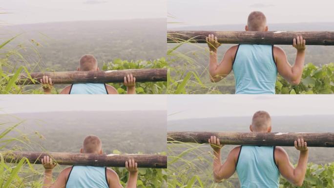 户外训练时，运动男子蹲在肩膀上的木制杠铃上。运动员在热带高地景观上训练用木料深蹲运动。户外健身房锻炼