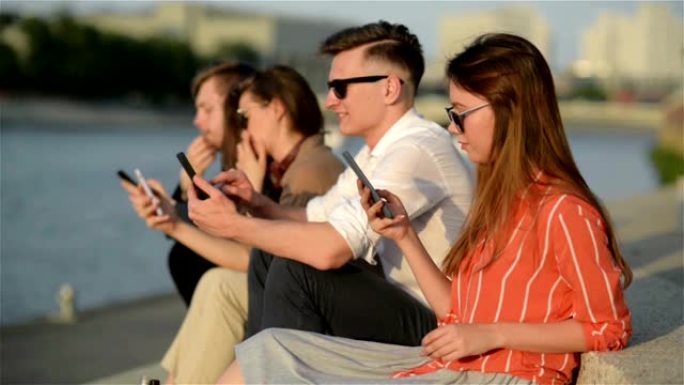 四个朋友在街上的智能手机中欢笑并观看社交媒体。每个人都有自己的电话。最好的朋友和学生在户外共度时光