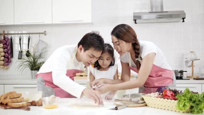 4k慢动作，年轻的亚洲父亲母亲和女儿在现代白色厨房中准备蛋糕混合物快乐而有趣。烹饪时开朗的女儿。