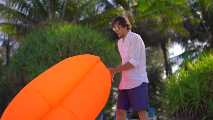 热带海滩上的年轻人给充气沙发充气。暑假概念